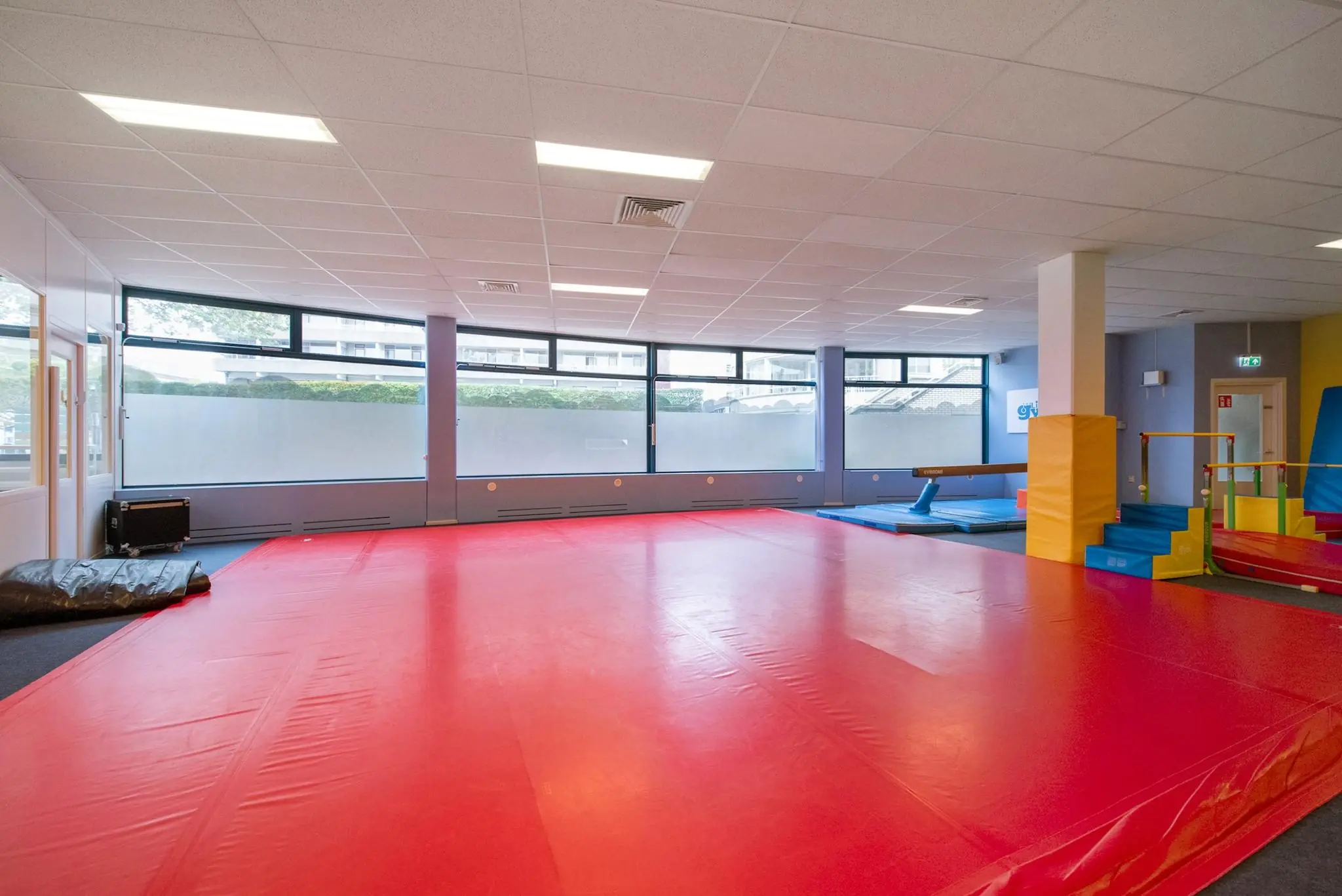 Gymzaal aan de Koningin Julianalaan met rode turnmatten, klimtoestellen en een evenwichtsbalk voor kinderactiviteiten.